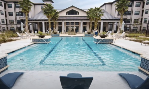 resort style pool with seating palm trees and a building behind it
